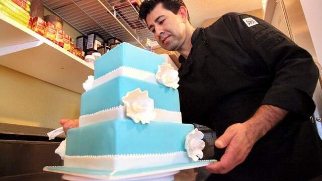 Let Them Eat Cake worker with finished cake with blue icing and white flowers