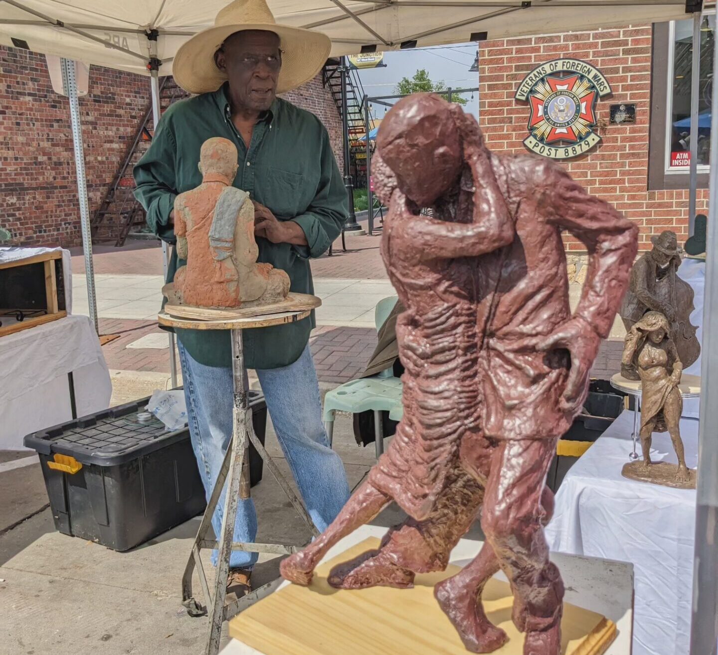 vendor at arts festival sculpting a figure with dancing couple sculpture int he foreground