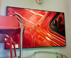 painting of a red classic car drivers door and front fender with a mid century chair in the forground